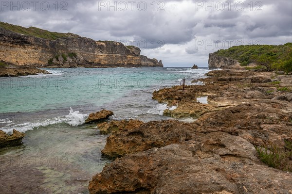 Rocky coast, long bay by the sea at sunset. Dangerous view of the Caribbean Sea. Tropical climate on a cloudy day in La Porte d'Enfer, Grande Terre, Guadeloupe, French Antilles, North America