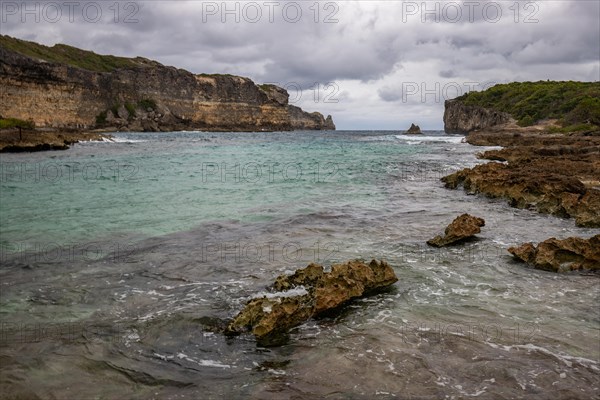 Rocky coast, long bay by the sea at sunset. Dangerous view of the Caribbean Sea. Tropical climate on a cloudy day in La Porte d'Enfer, Grande Terre, Guadeloupe, French Antilles, North America