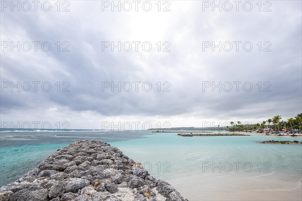 Caribbean dream beach with palm trees, white sandy beach and turquoise-coloured, crystal-clear water in the sea. Shallow bay on a cloudy day. Plage de Sainte Anne, Grande Terre, Guadeloupe, French Antilles, North America