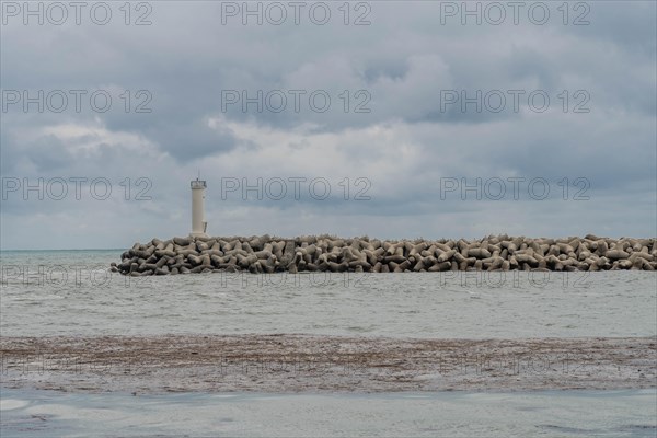 White lighthouse on a protective stone breakwater jutting out into a cloudy sea, in Ulsan, South Korea, Asia