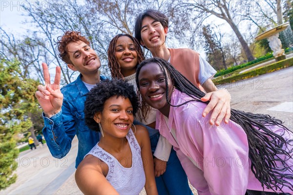 Frontal three quarter length portrait of five cute young multiracial friends talking selfie in a park