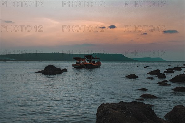 Scenic view of two Khmer fishing boats in mooring on the rocky coast of Koh Rong Island in Cambodia during sunset