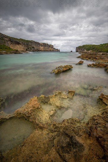 Rocky coast, long bay by the sea at sunset. Dangerous view of the Caribbean Sea. Tropical climate on a cloudy day in La Porte d'Enfer, Grande Terre, Guadeloupe, French Antilles, North America