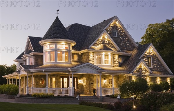Elegant grey stone with white trim and blue asphalt shingles roof Victorian home facade at dusk in summer, Quebec, Canada, North America