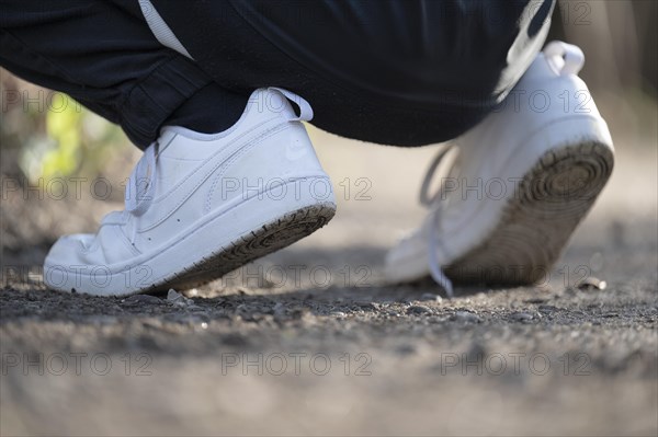 White trainers of an athletically dressed boy, crouched posture, on a gravel path, sole visible, at eye level, Germany, Europe