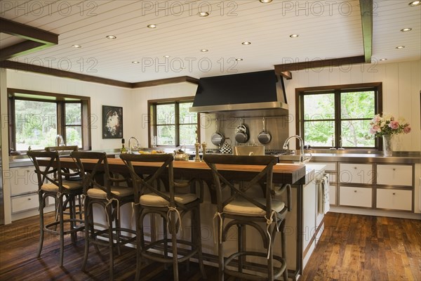Country style kitchen with island and rustic wooden high chairs inside New Hampton style home, Quebec, Canada, North America