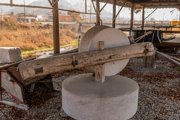 Old antique millstone and wheel in covered shelter with mountain community in background in South Korea