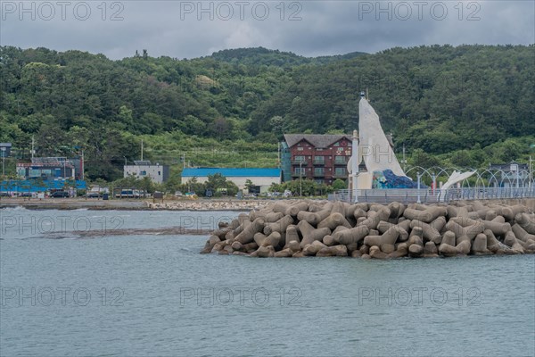 Ocean view of a landmark sculpture at the end of a pier, with greenery and a cloudy sky, in Ulsan, South Korea, Asia