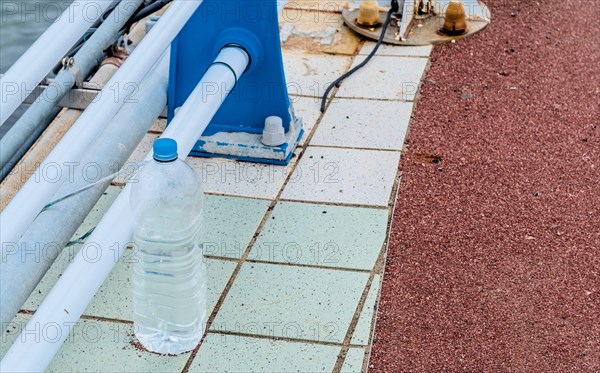 Discarded plastic bottle beside a metal railing on a mosaic tiled waterfront walkway, in Ulsan, South Korea, Asia