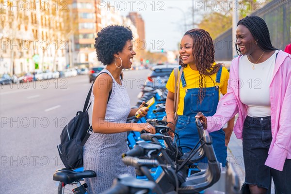 Three african young happy friends renting public bike using phone in the city