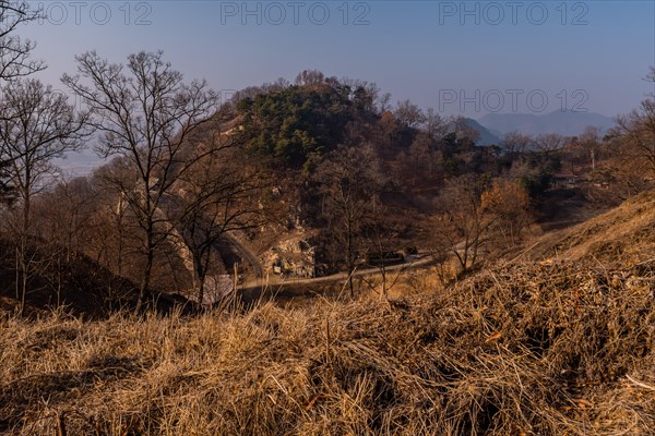 Section of mountain fortress wall behind leafless trees on top on winter morning with clear blue sky in background in Boeun, South Korea, Asia