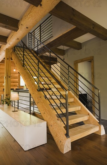 Wooden log stairs with black wrought iron railings and long cabinet table inside contemporary style log home, Quebec, Canada, North America