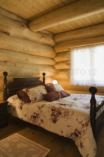 Antique four poster queen size bed with floral motifs bedspread in guest bedroom inside handcrafted Eastern white pine Scandinavian log cabin home, Quebec, Canada, North America