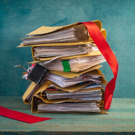 A large pile of files, bound with a red ribbon, on a wooden table in front of a blue wall, symbolising bureaucracy, AI generated, AI generated