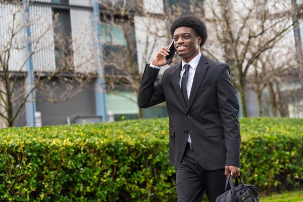 Three quarter length portrait of a cool smiling african businessman walking along the street using phone