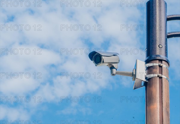 Surveillance camera mounted on metal light pole with blue sky and puffy white clouds in background in South Korea