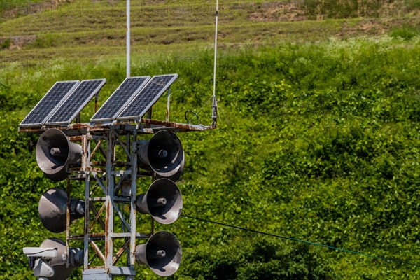 Communication tower consisting of loud speakers, solar panel and closed circuit camera with tree covered mountain in background in South Korea