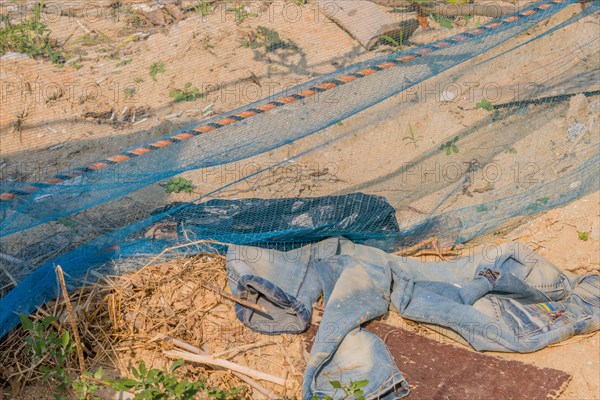 Abandoned clothing and construction net against dry soil depicting waste and negligence, in South Korea