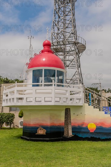 A red lighthouse replica in front of a communication tower under a clear sky, in Ulsan, South Korea, Asia