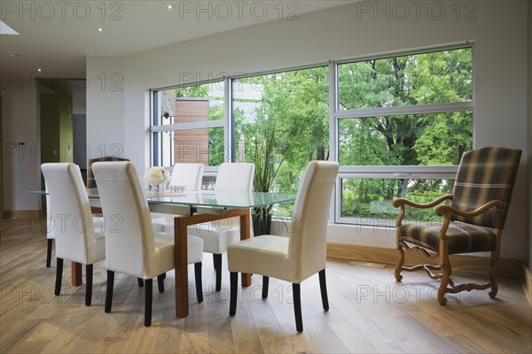 Clear glass top table with white leather high back chairs in dining room with beige ceramic tile floor inside modern cubist style home, Quebec, Canada, North America