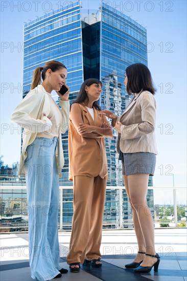 Low-angle view of three colleagues on a coffee break. One of them is talking on her cell phone while the others are chatting
