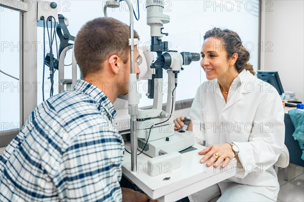 Friendly female ophthalmologist examining a man's eyes with a slit lamp in the clinic