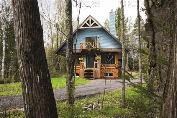 Post and beam cottage style hybrid log home facade with blue clapboard trim and timber elements in spring, Quebec, Canada, North America