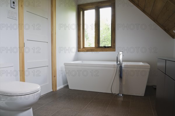Main bathroom with grey ceramic tile floor and white porcelain toilet and freestanding bathtub on upstairs floor inside contemporary style log home, Quebec, Canada, North America