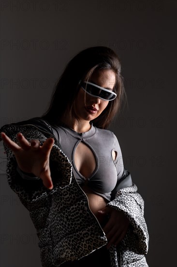 Studio portrait with grey background of a futuristic woman gesturing wearing elegant clothes and VR goggles