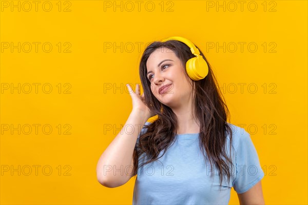 Studio portrait with yellow background of a cute woman listening to music with wireless headphones