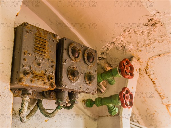 Closeup of rusted electrical circuit boxes and pressure valves with red handles attached to green metal fittings in Gangneung, South Korea, Asia