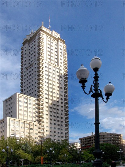 A skyscraper rises into the blue sky, next to a classic street lamp and surrounded by greenery Madrid Spain