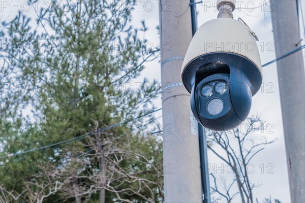 Closeup of round black surveillance camera in front of utility poles with blurred background in South Korea