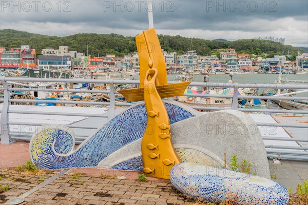 A colorful mosaic fish sculpture at a harbor with boats and a cloudy sky in the background, in Ulsan, South Korea, Asia