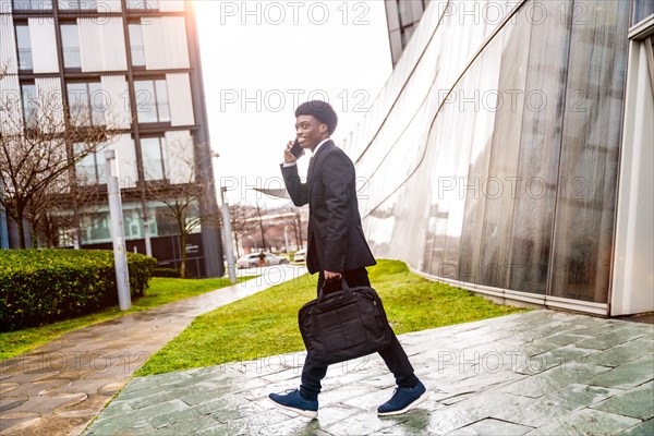 African businessman talking with mobile while commuting to work walking along the street