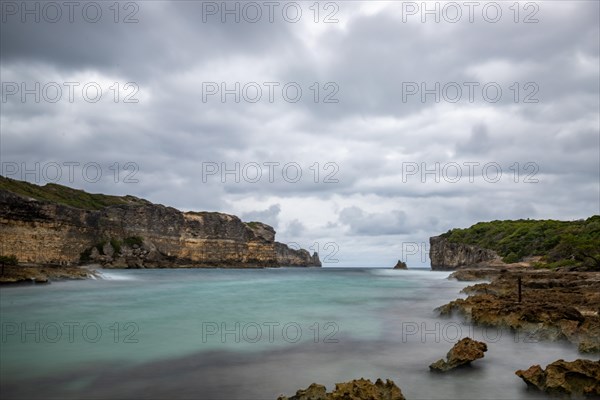 Rocky coast, long bay by the sea at sunset. Dangerous view of the Caribbean Sea. Tropical climate on a cloudy day in La Porte d'Enfer, Grande Terre, Guadeloupe, French Antilles, North America