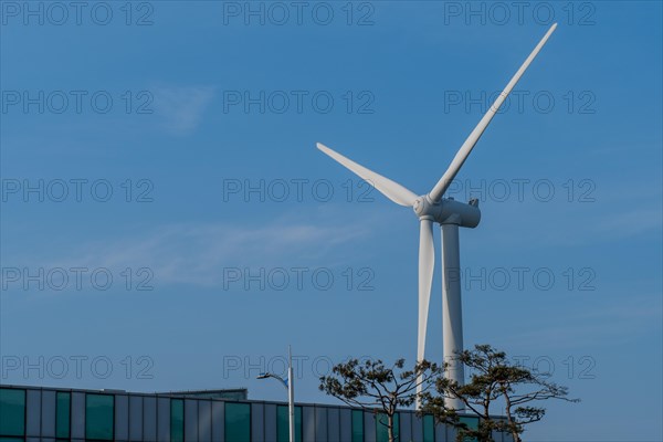 Close up of wind turbine blades above a building with blue sky in background in South Korea