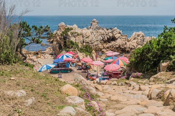 A rocky beach area with colorful umbrellas and tourists enjoying the seaside, in Ulsan, South Korea, Asia