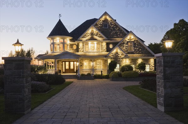 Elegant grey stone with white trim and blue asphalt shingles roof Victorian home facade at dusk in summer, Quebec, Canada, North America