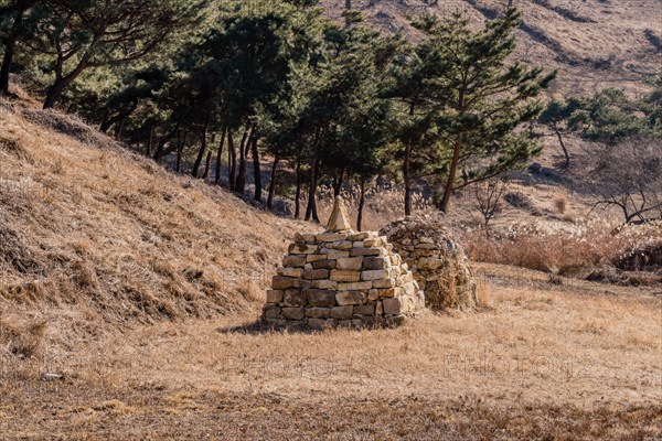 Two pyramid shaped rock structures in field of brown grass at foot of hillside in Boeun, South Korea, Asia