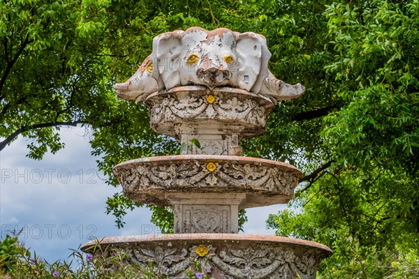 Ornate weathered fountain adorned with flowers and surrounded by green trees, in Chiang Mai, Thailand, Asia