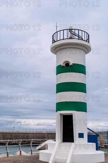 A lighthouse with green stripes stands against an overcast sky near the ocean, in Ulsan, South Korea, Asia