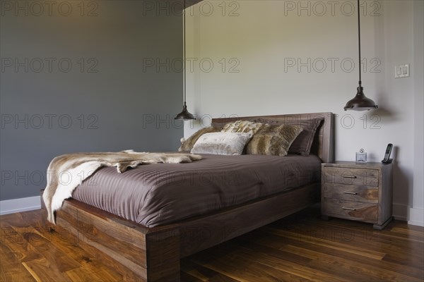 Queen size wooden base bed covered with fur pelt throw in guest bedroom inside luxurious home, Quebec, Canada, North America