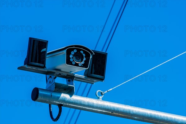 Closeup of closed circuit camera mounted on metal pole against light blue sky in background in South Korea