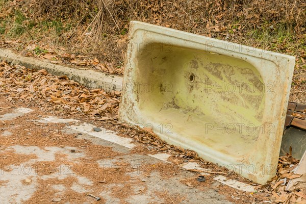 An old, dirty bathtub left upside down beside a path with leaves, in South Korea