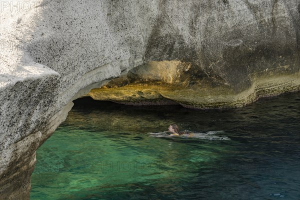 A girl swims under a stone bridge by the white rocks on the coast at Sarakinikoer, Milos, Cyclades, Greece, Europe