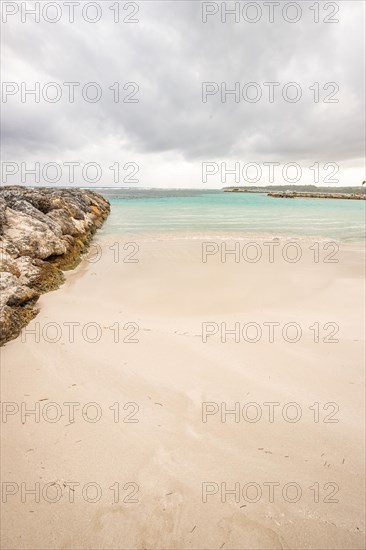 Caribbean dream beach with palm trees, white sandy beach and turquoise-coloured, crystal-clear water in the sea. Shallow bay on a cloudy day. Plage de Sainte Anne, Grande Terre, Guadeloupe, French Antilles, North America