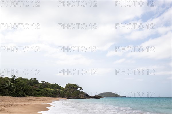 Lonely, wide sandy beach with turquoise-coloured sea. Tropical plants in a bay in the Caribbean sunshine. Plage de Cluny, Basse Terre, Guadeloupe, French Antilles, North America