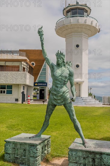 Statue in a hero pose with a lighthouse and a dramatic sky in the background, in Ulsan, South Korea, Asia