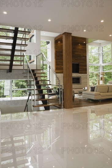 Wood, metal and glass staircase leading to living room with creamy beige L-shaped leather sofa inside luxurious home, Quebec, Canada, North America